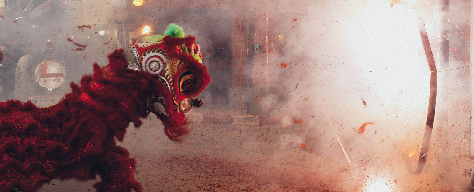 A red chinese lion dancer next to smoke from fireworks 