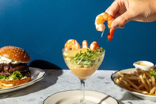 Meals from The Independent presented on small plates with a hand grabbing a prawn